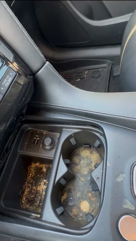 Dirty vehicle center console with spilled liquid and debris in cup holders before detailing