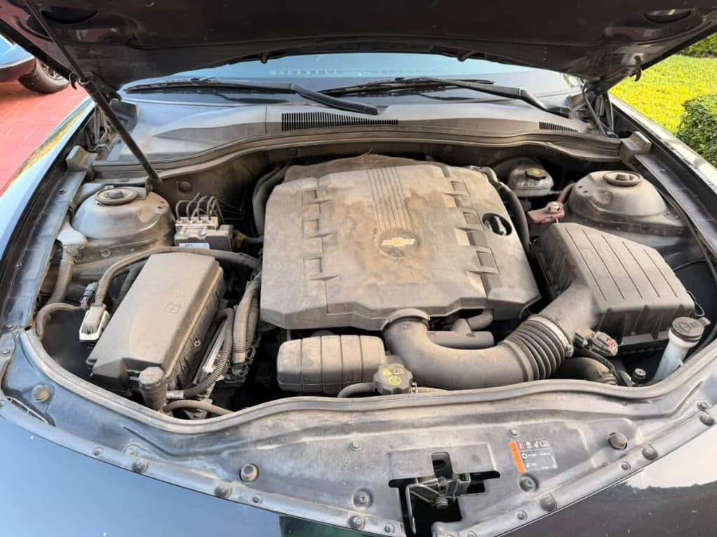 Dusty Chevrolet engine bay with bowtie emblem on the cover before cleaning