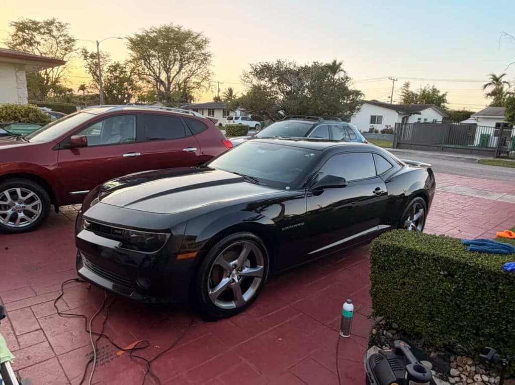 Black Chevrolet Camaro on a red tiled driveway at golden hour with detailing supplies nearby